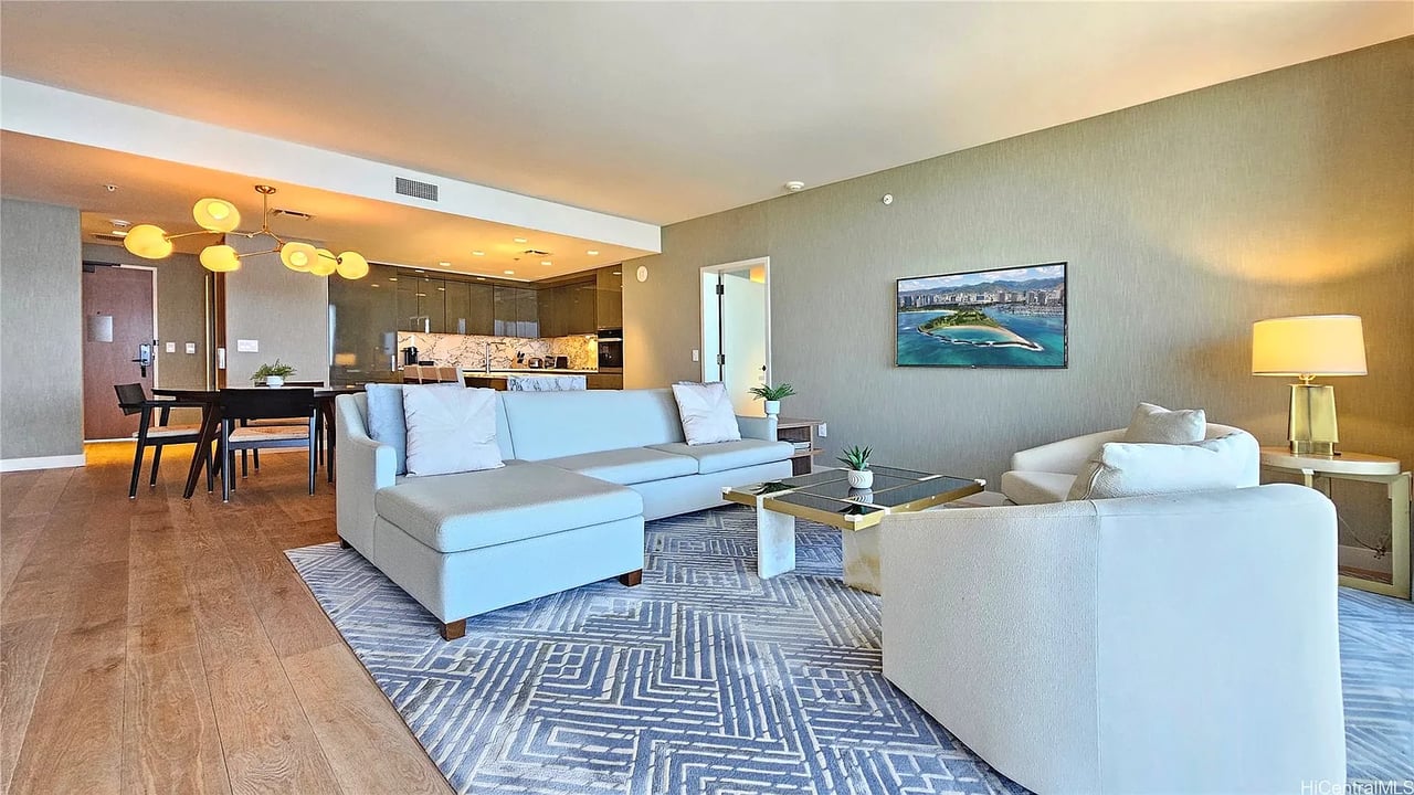 Living room with pale sofas, a geometric rug, and an open dining area and kitchen.