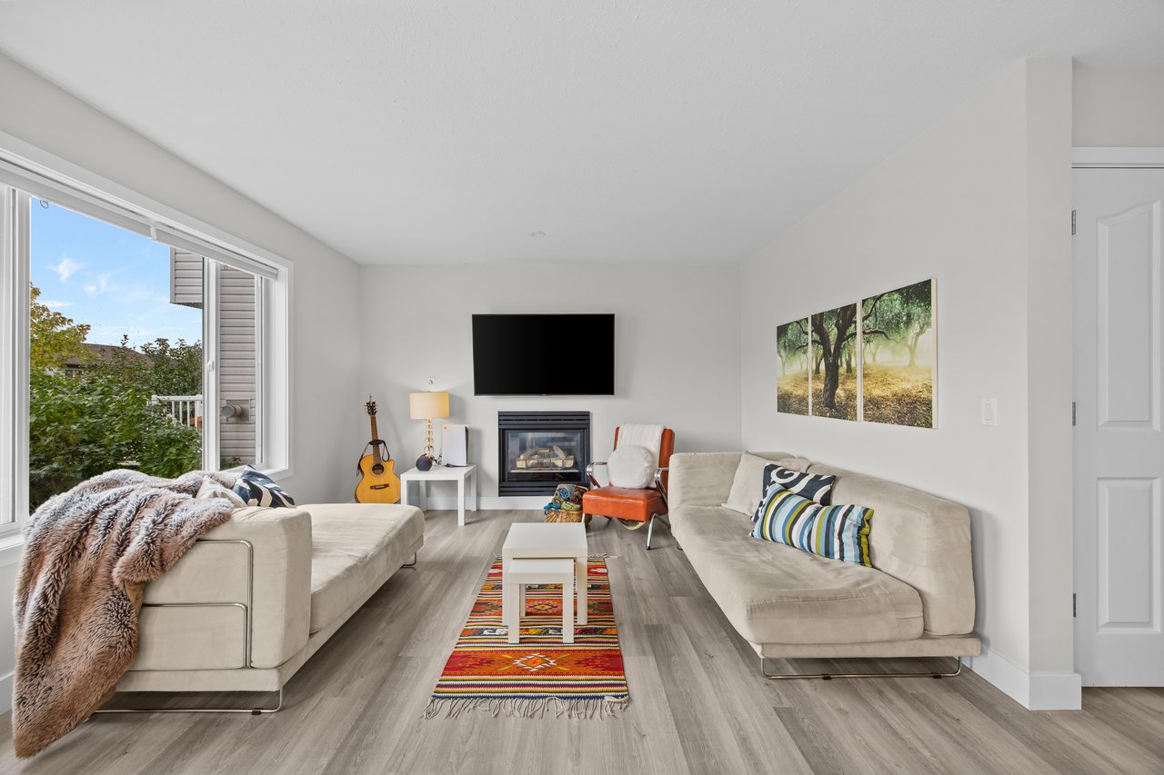 Living room with cream sofas, a fireplace, large windows, and a colorful rug.