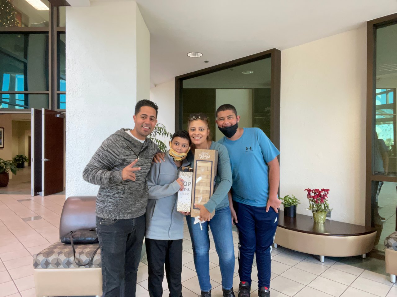 Four people pose with gift baskets in a lobby; one wears a mask and another has one lowered.