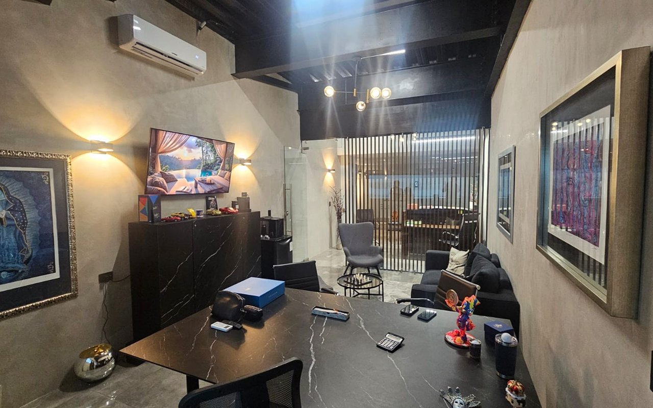 Furnished office with a black marble conference table and a glass meeting room behind vertical slats.