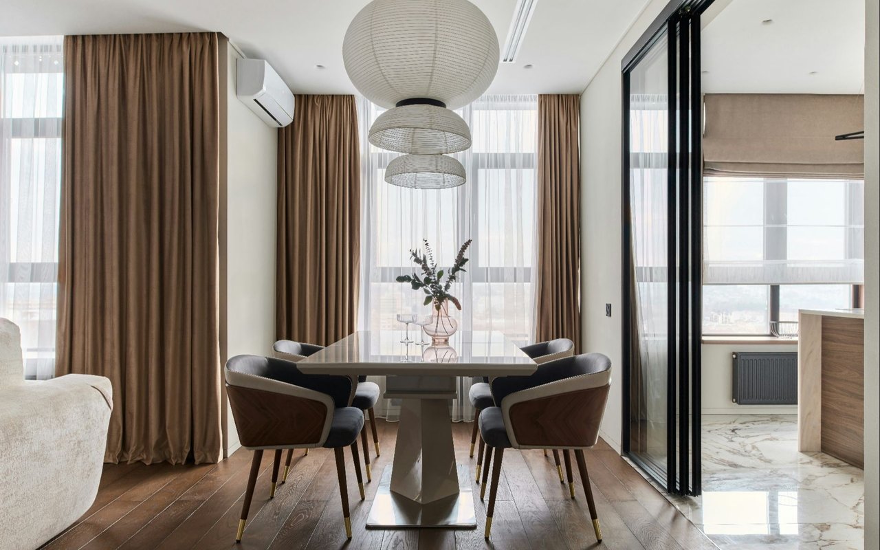 Modern dining room with sculptural pendant lights, brown curtains, and floor-to-ceiling windows.