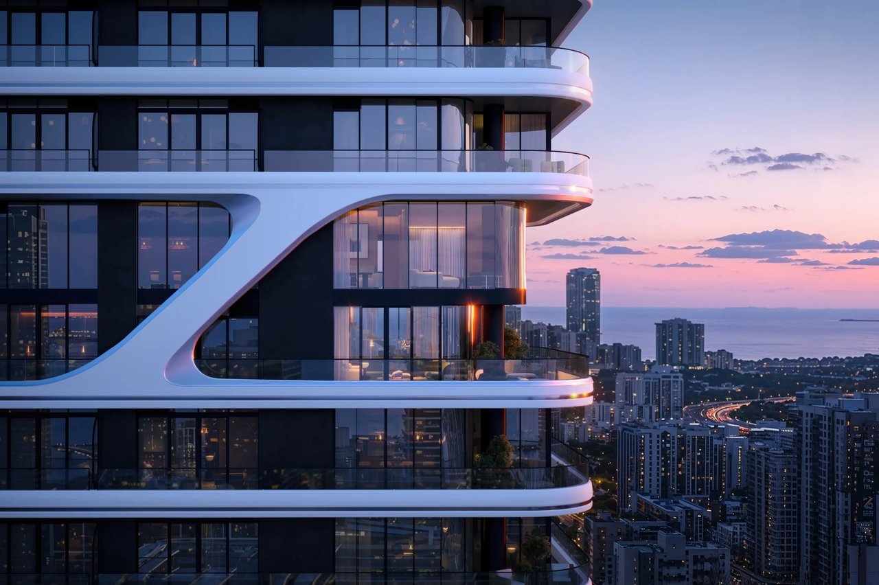 Modern high-rise tower with sweeping balconies overlooking a coastal city at sunset.