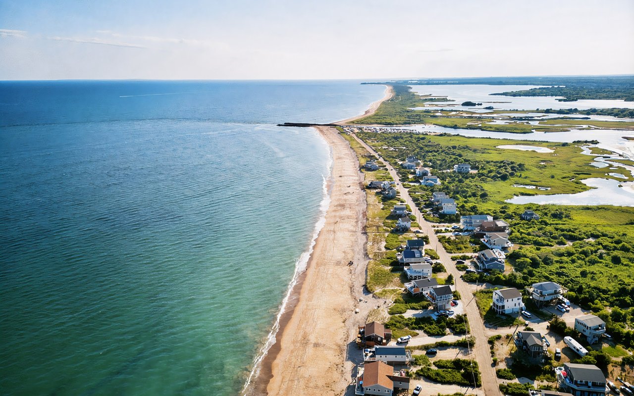 Coastal neighborhood of houses along a sandy beach beside salt marshes.