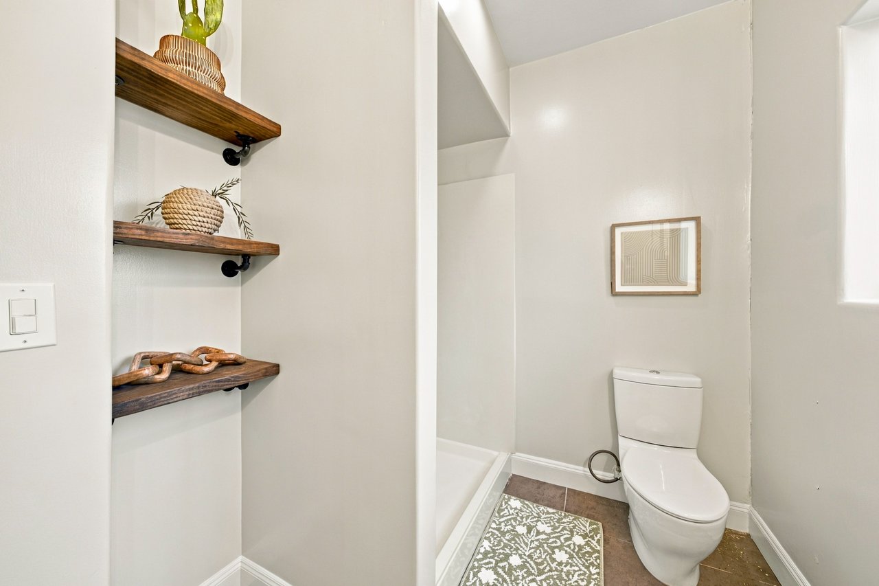 Bathroom with a white toilet, shower, and dark wood display shelves.