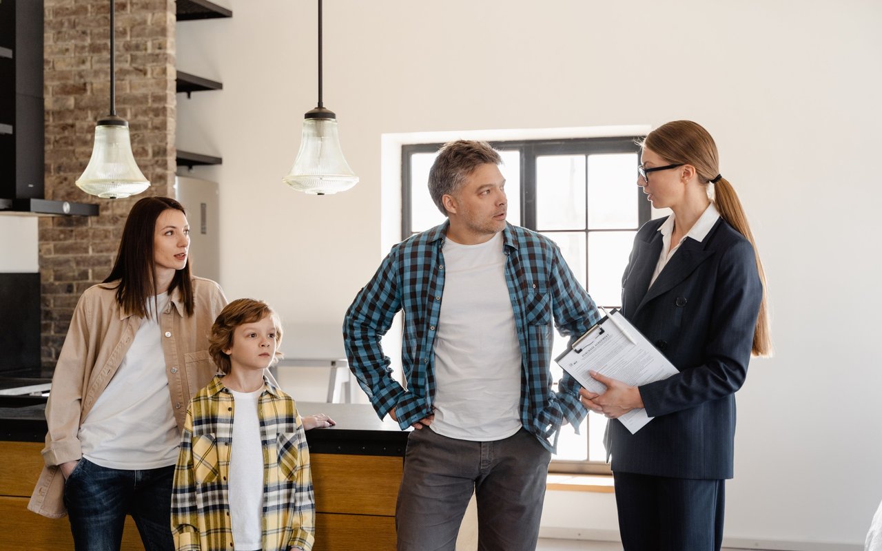 Family talks with a real estate agent in a kitchen beside a wood island and brick backsplash.