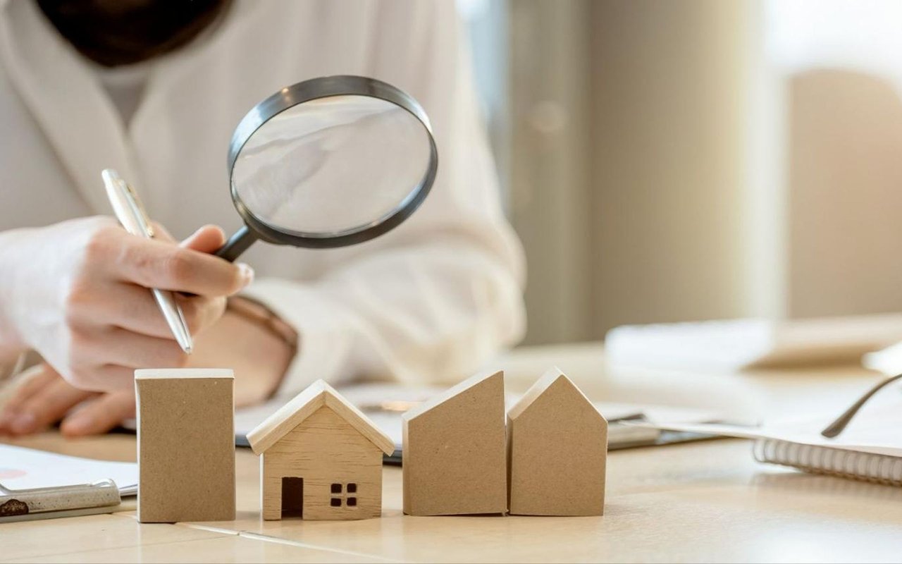 Person examines cardboard model houses with a magnifying glass and pen.