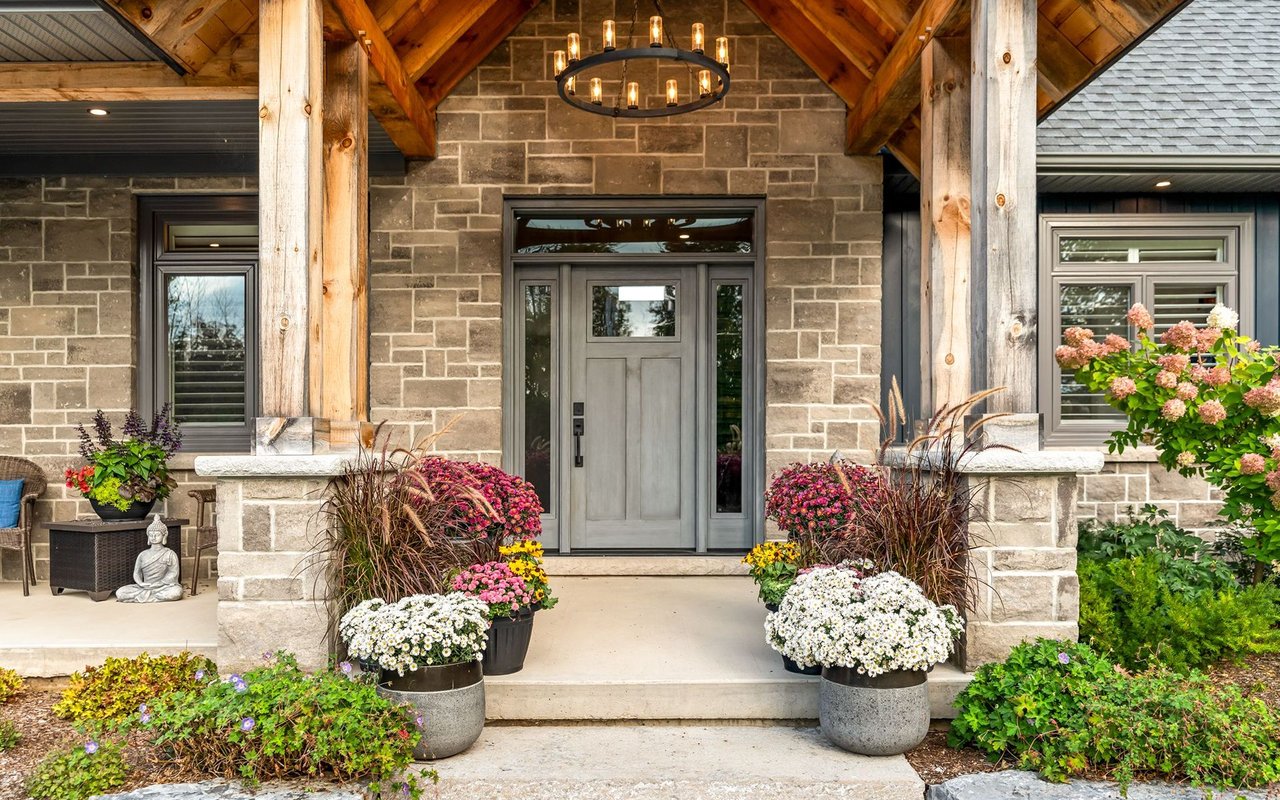 Stone home entrance with gray door, timber porch beams, and colorful flower planters.