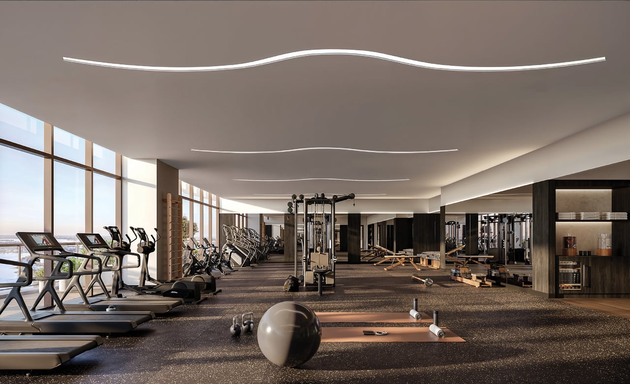 Residential fitness center with treadmills, strength machines, and a stretching area beside tall windows.