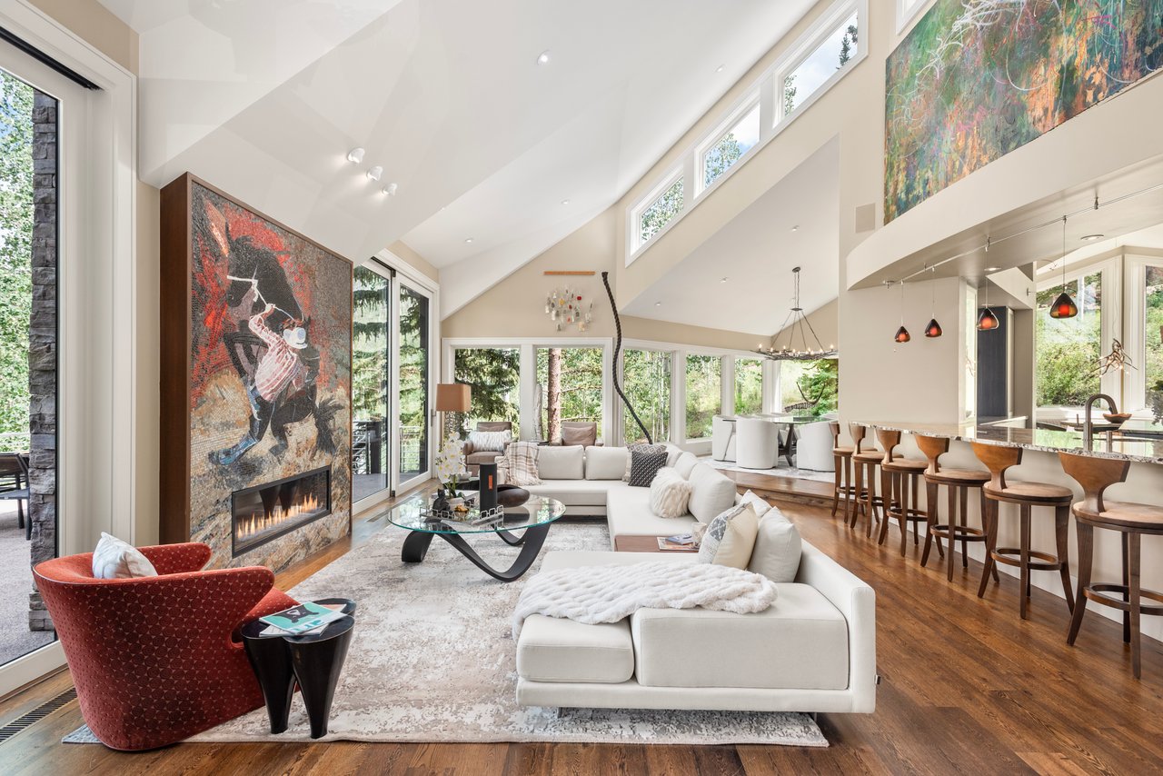 Vaulted living room with a white sectional, red chairs, and a striking fireplace mural.