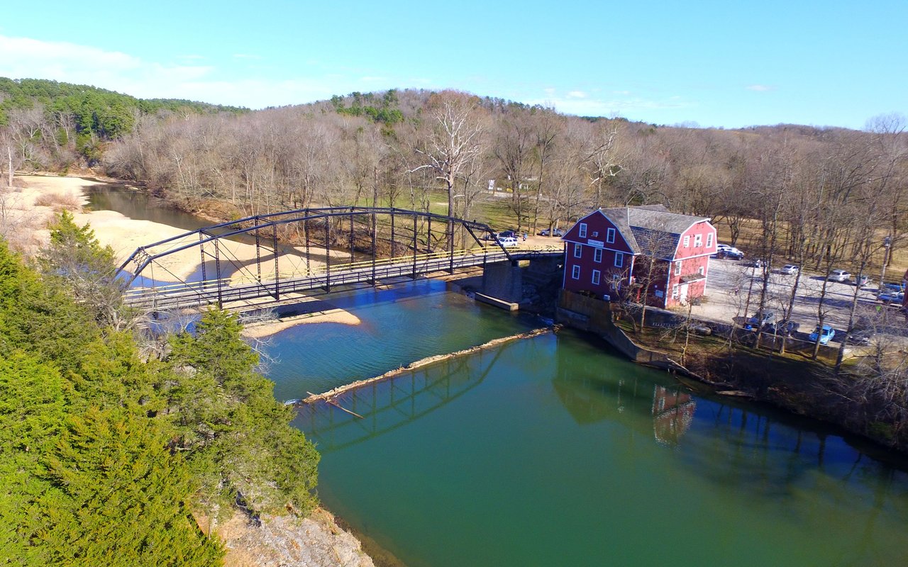 Aerial view of a metal bridge and red building beside a river.