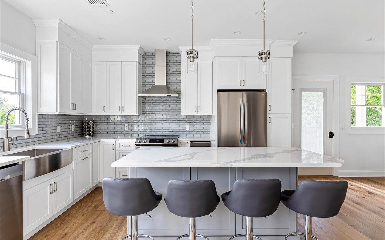 White kitchen with gray tile backsplash, stainless appliances, and an island with four stools.