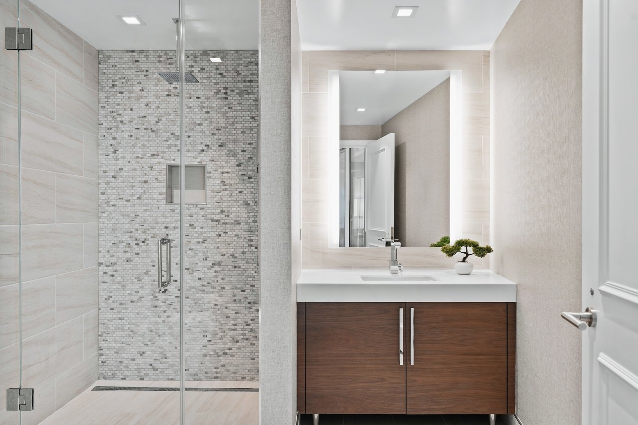 Modern bathroom with a gray mosaic-tile shower and dark wood vanity beneath a wide mirror.