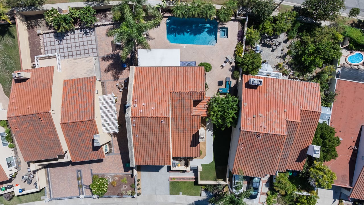 Aerial view of neighboring homes with red tile roofs and swimming pools.