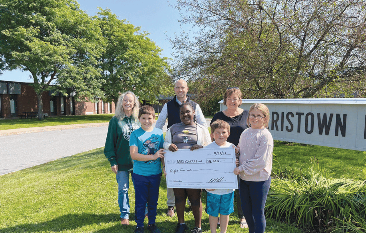 Seven adults and children pose with an $8,000 donation check beside a Bristown sign.