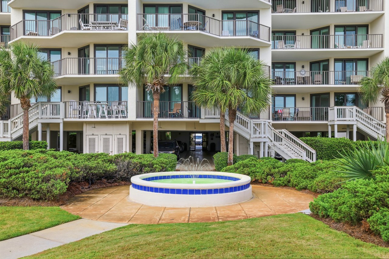 Multi-story villa building with palm-lined balconies and a circular fountain pool in front.