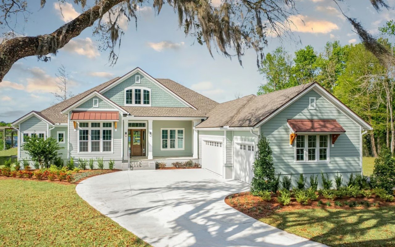 Sage-green house with red window awnings, an attached garage, and a curved driveway.