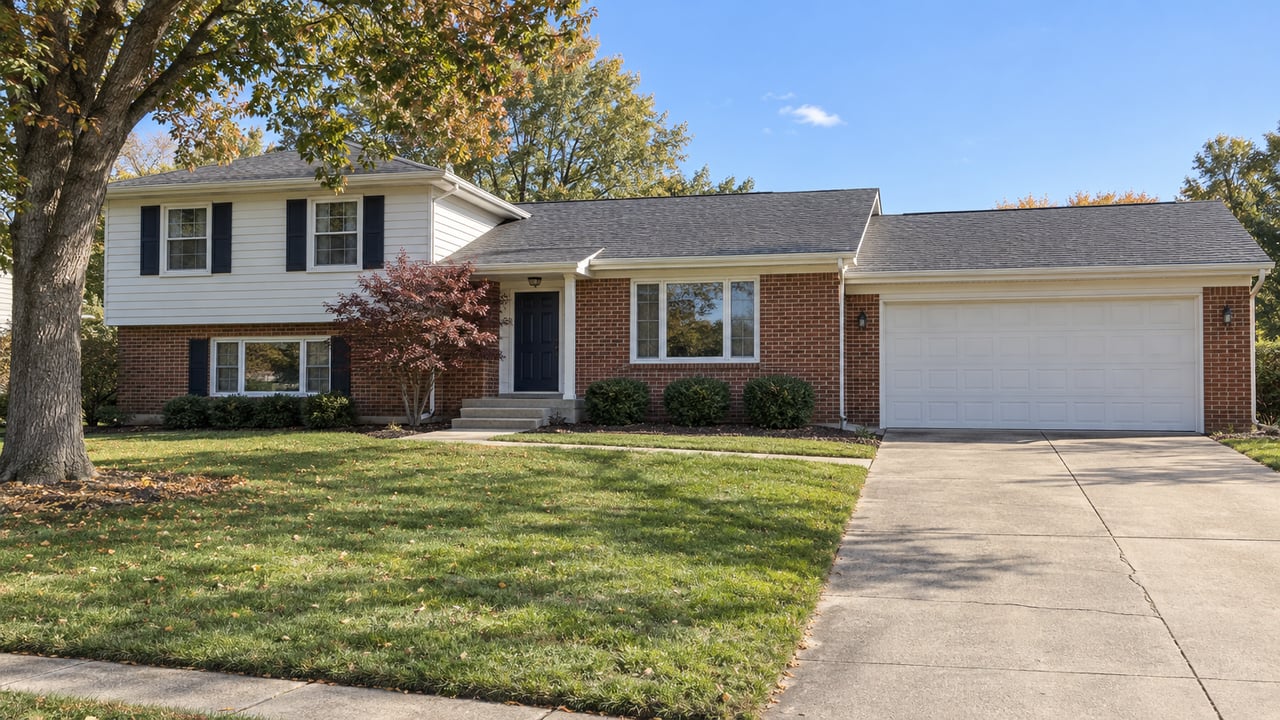 Brick-and-white-siding split-level home with a broad front lawn, concrete driveway, double garage and autumn foliage.