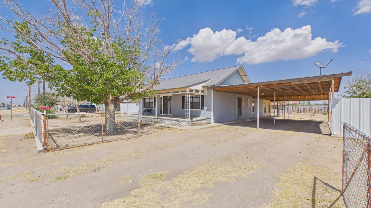 House with a metal-roofed carport, chain-link fencing, and a large tree in the front yard.