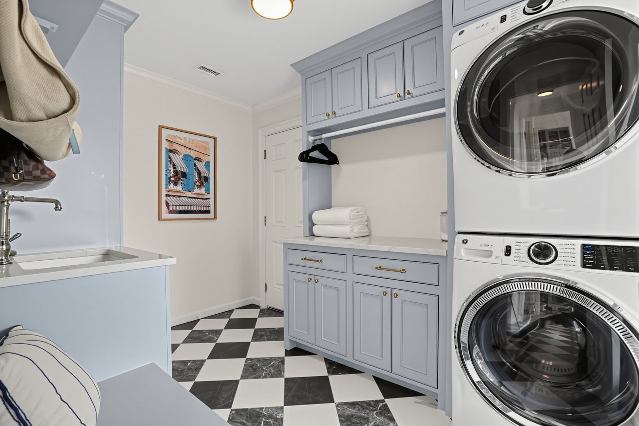 Laundry room with stacked washer and dryer, pale blue cabinetry, and checkerboard tile floor.