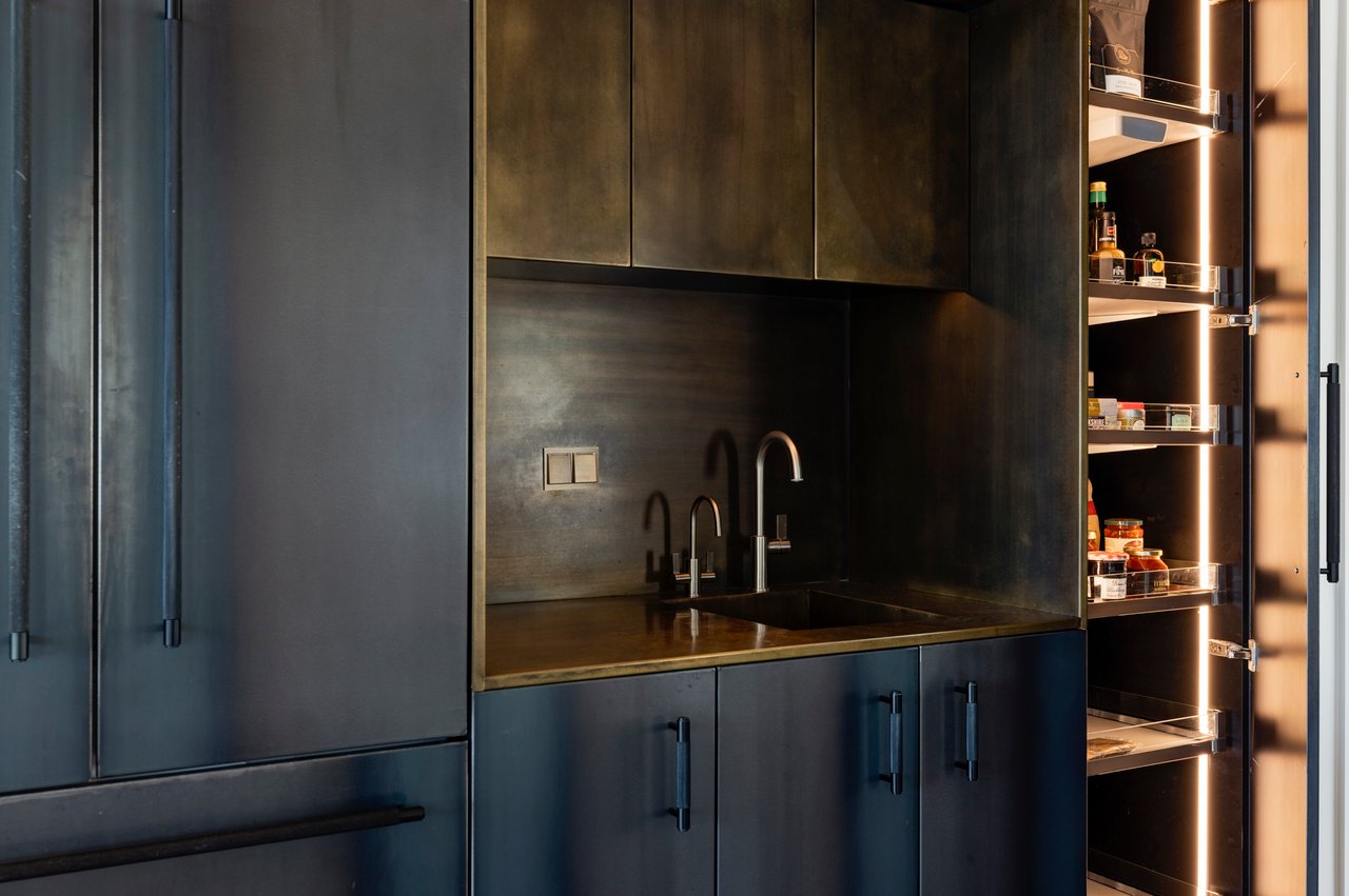 Modern Boulder kitchen bar with black metal cabinets, brass backsplash, and illuminated pantry shelving