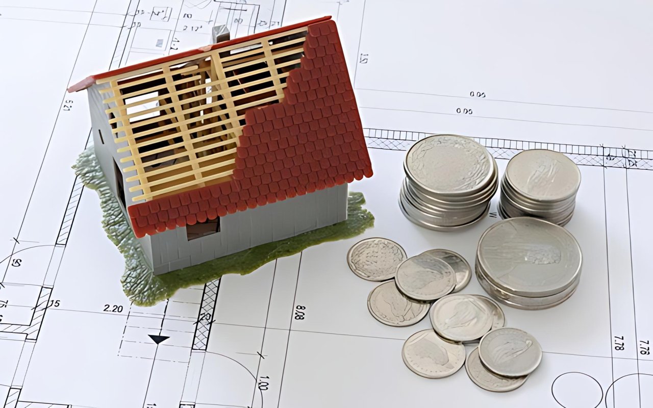 Model house with an exposed roof frame and coins on architectural plans.