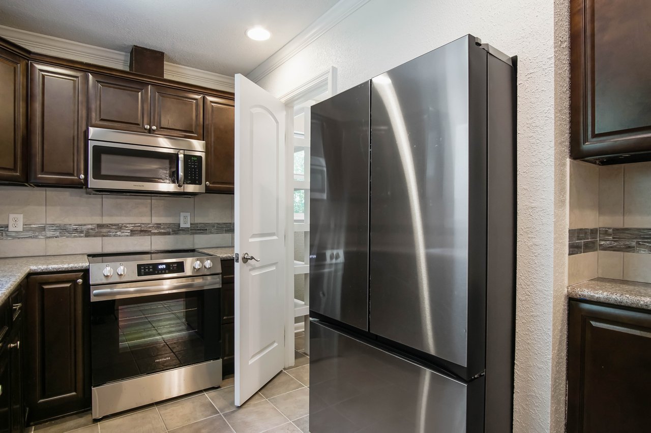 Modern kitchen with stainless steel appliances, including a fridge and oven. Dark wooden cabinets and open door create a warm, inviting atmosphere.