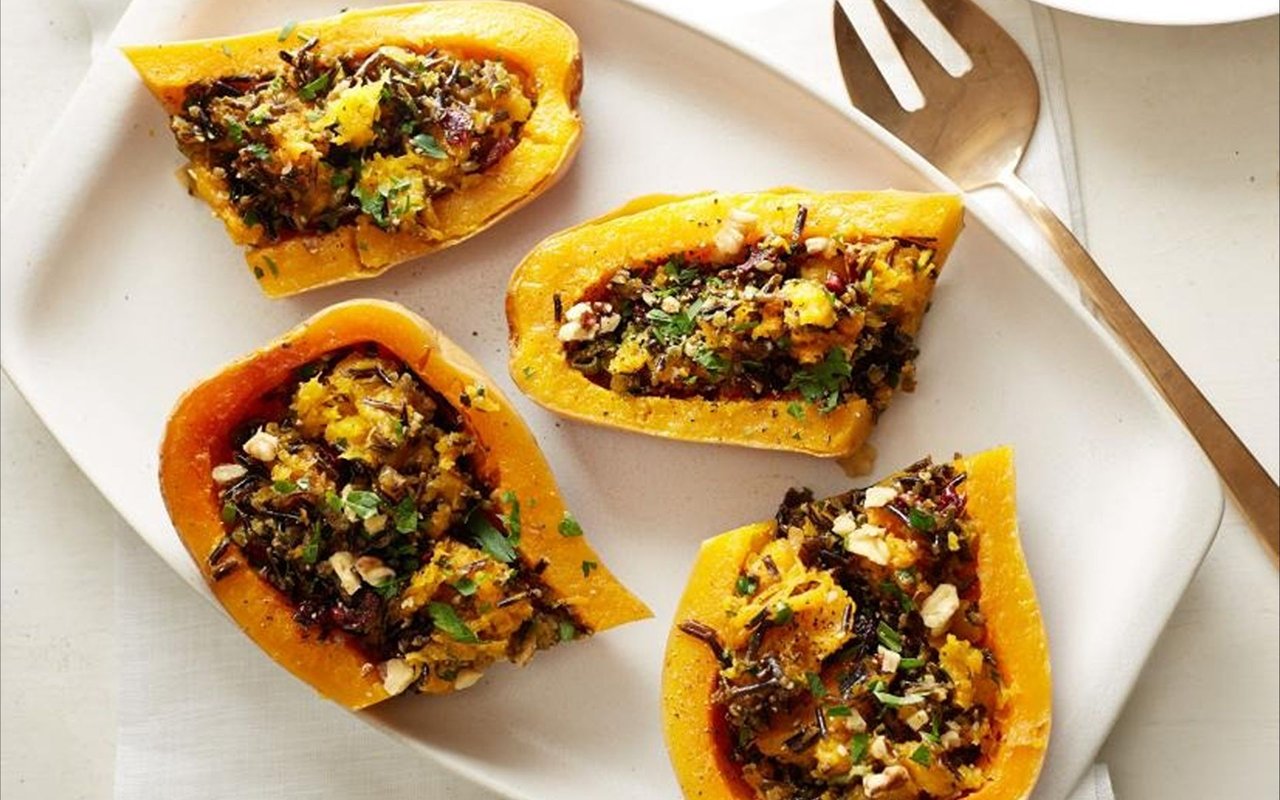 Roasted squash halves stuffed with grains, nuts, dried fruit, and herbs on a white plate.