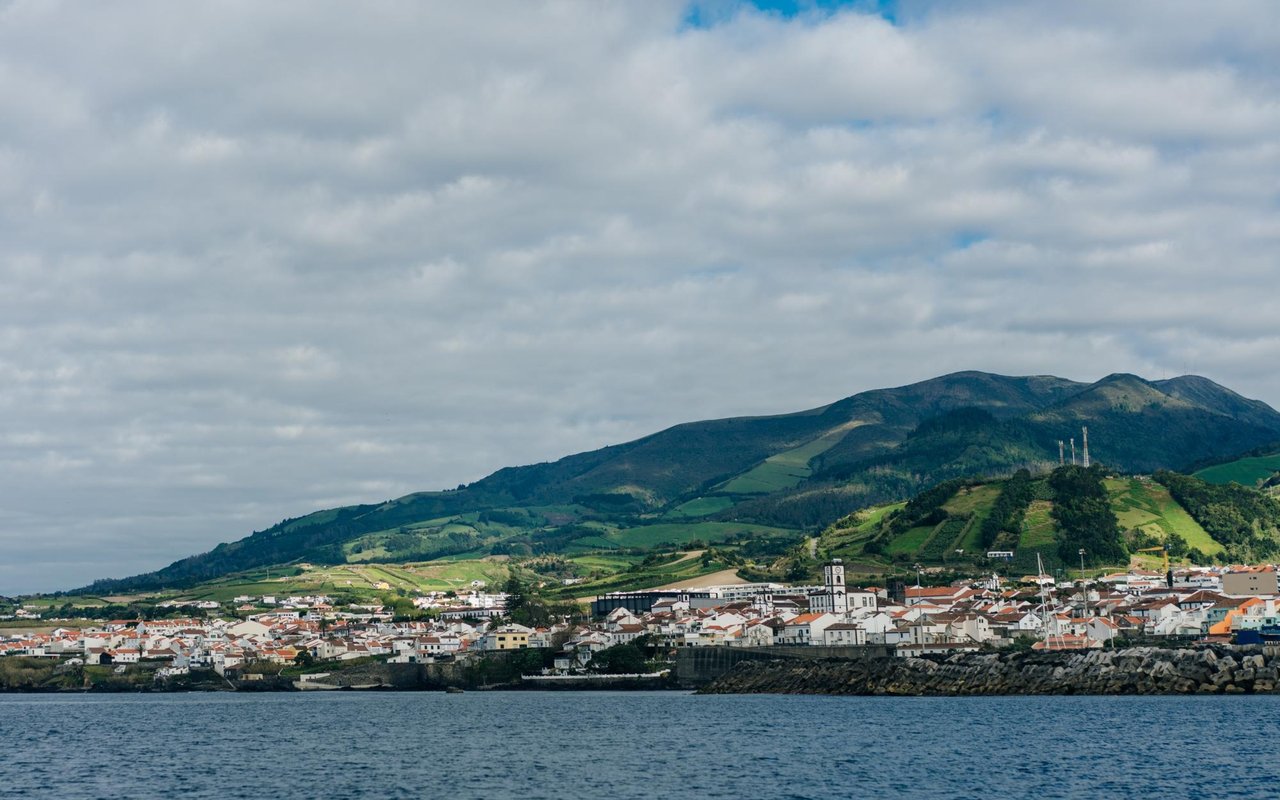 Coastal town beside blue water, backed by green hills and mountains.