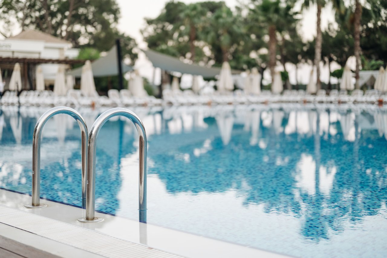 Outdoor swimming pool with a metal ladder and rows of lounge chairs and umbrellas.