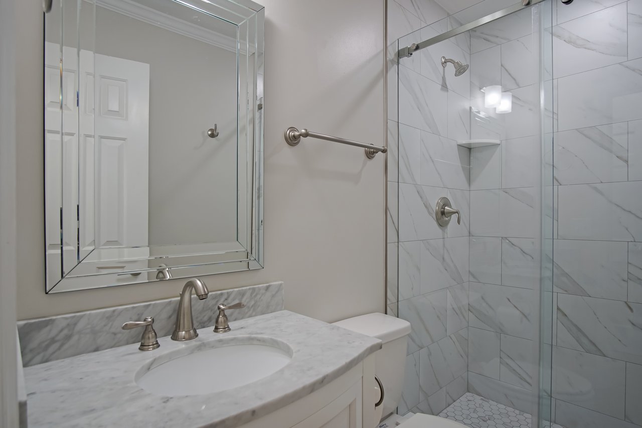Sleek bathroom with a marble countertop, elegant silver fixtures, and a large mirrored cabinet. Glass-door shower with marble tiles creates a modern, clean feel.