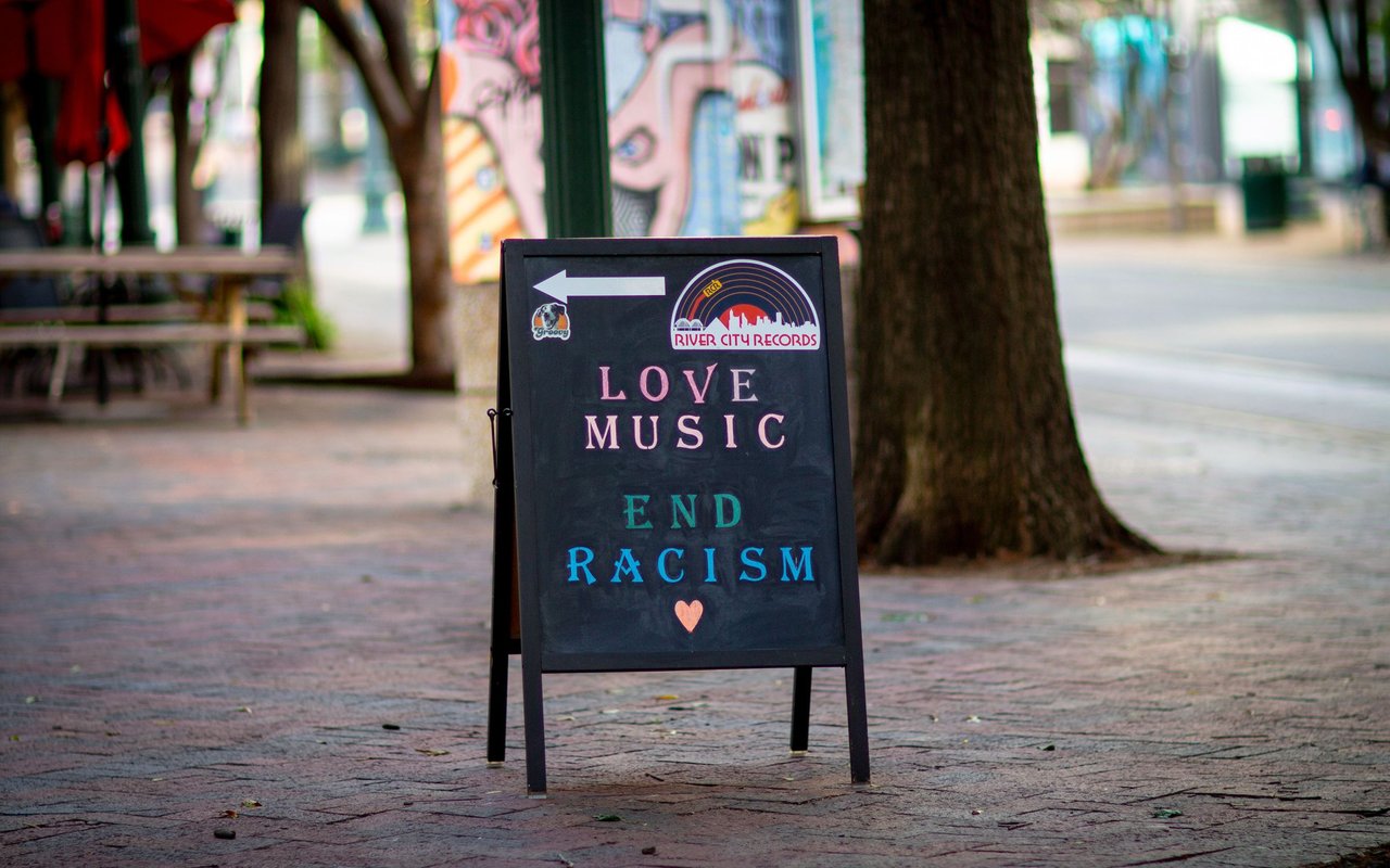 Sidewalk sign reading “Love Music, End Racism” points toward River City Records.