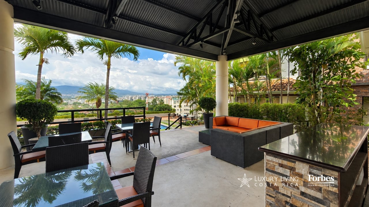 Covered terrace with outdoor dining and orange-cushioned seating overlooking the city and distant mountains.