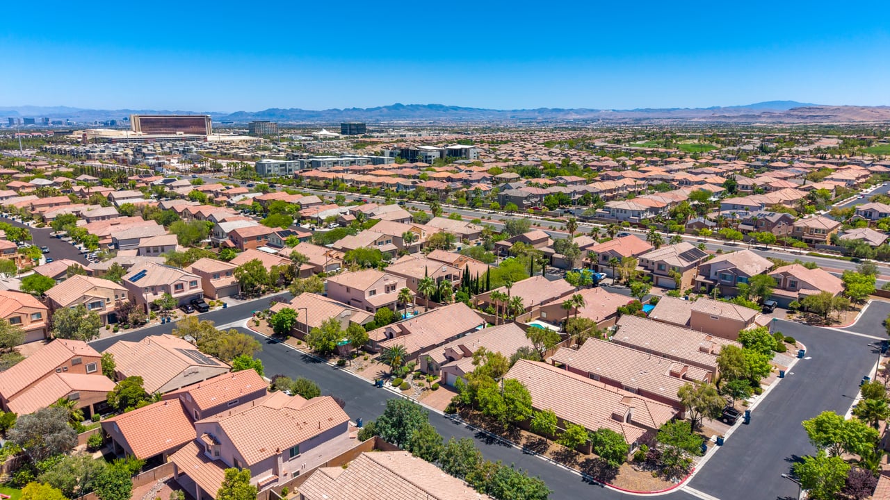 Aerial view of a terracotta-roofed neighborhood, with a distant city and mountains.
