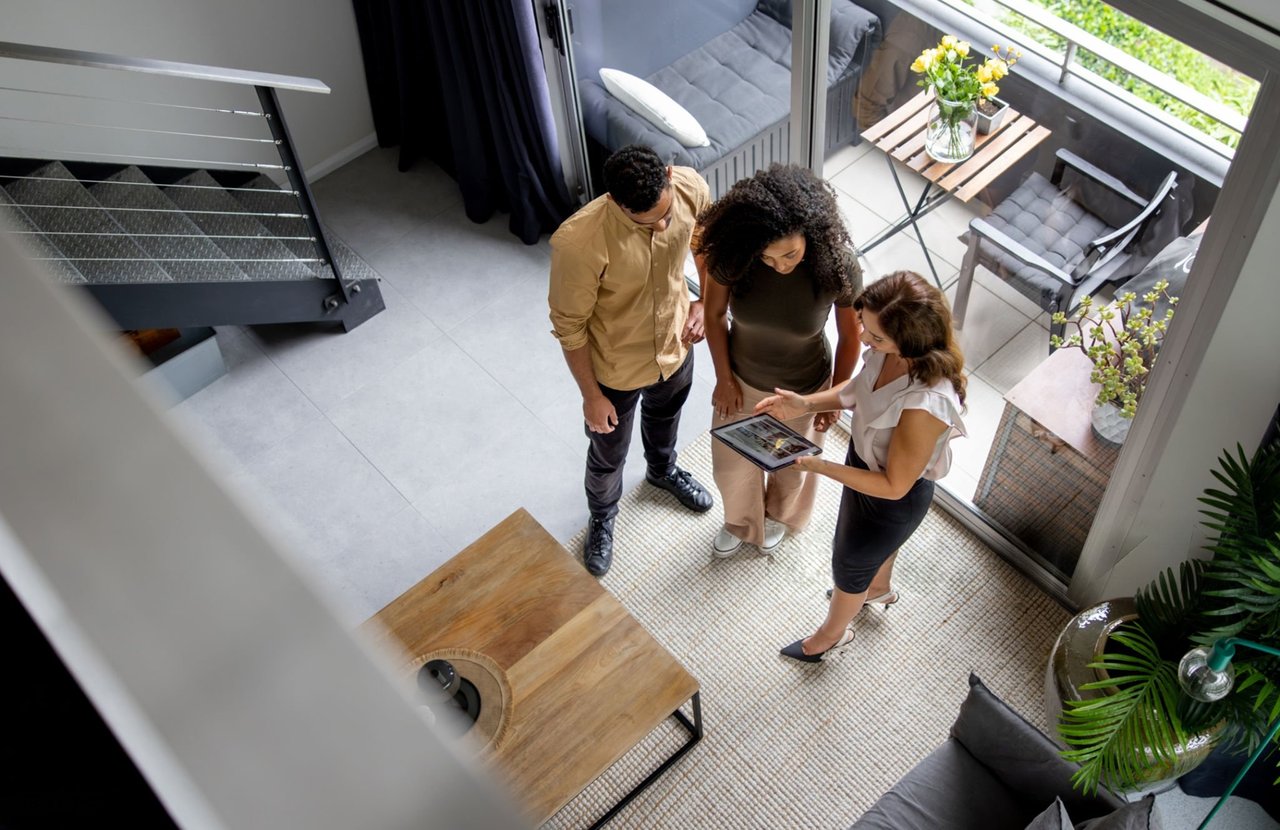 Three people review a tablet in a bright modern home's living room.
