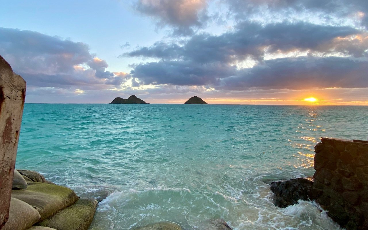 Turquoise water and rocky shoreline at sunset, with the Mokulua islets on the horizon.