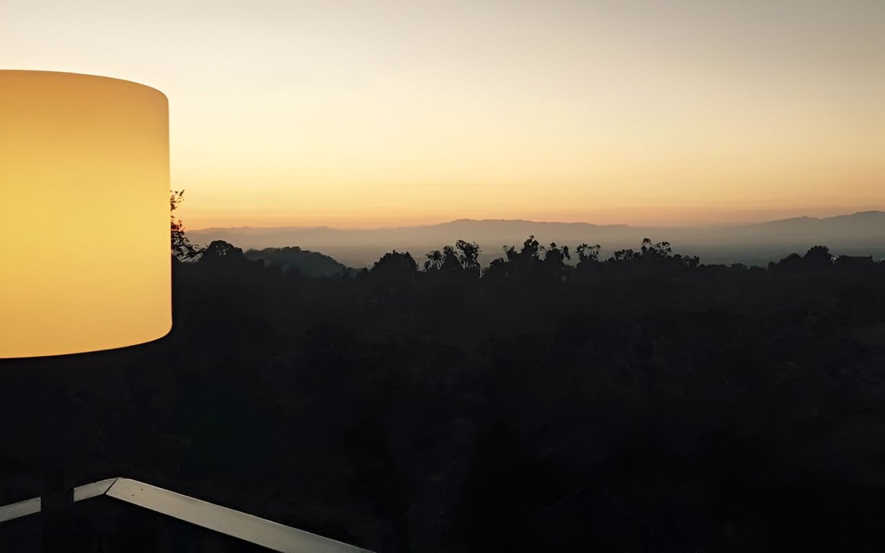 Sunset over distant hills, framed by a glowing cylindrical lamp at the left edge.