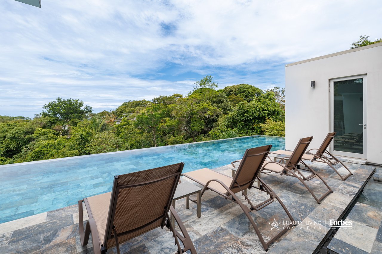 Infinity pool and stone terrace with lounge chairs overlooking dense tropical greenery.