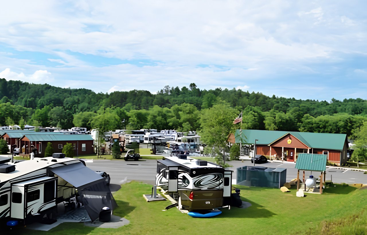 RV campground with parked motorhomes, cabins, and wooded hills beyond.