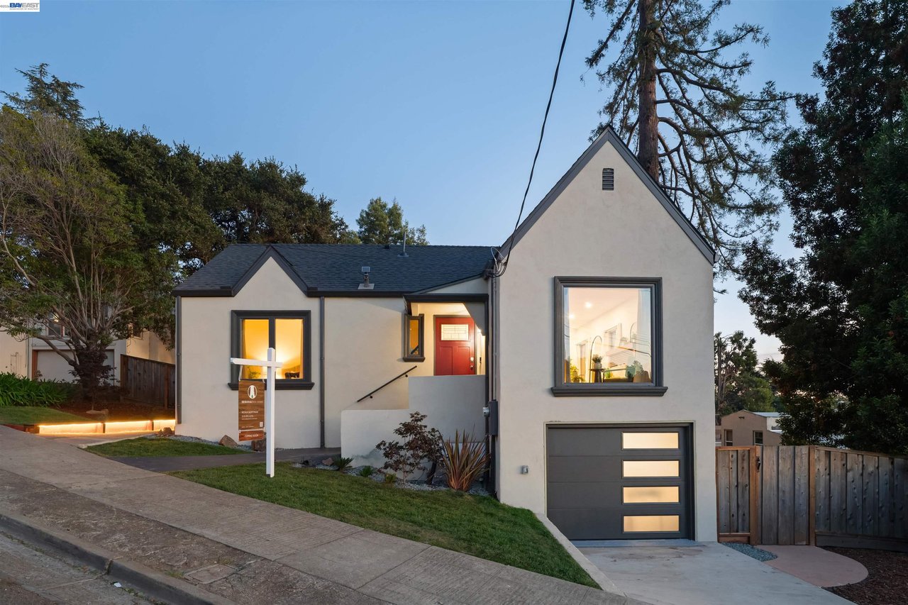 Oakland home with steep front gables, a red entry door, and an attached garage at dusk.