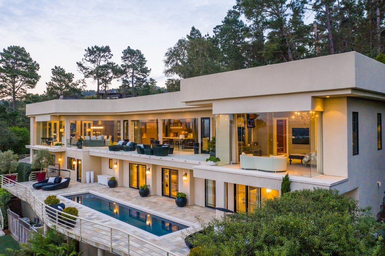 Modern glass-fronted home with a long pool and lounge terrace at dusk.