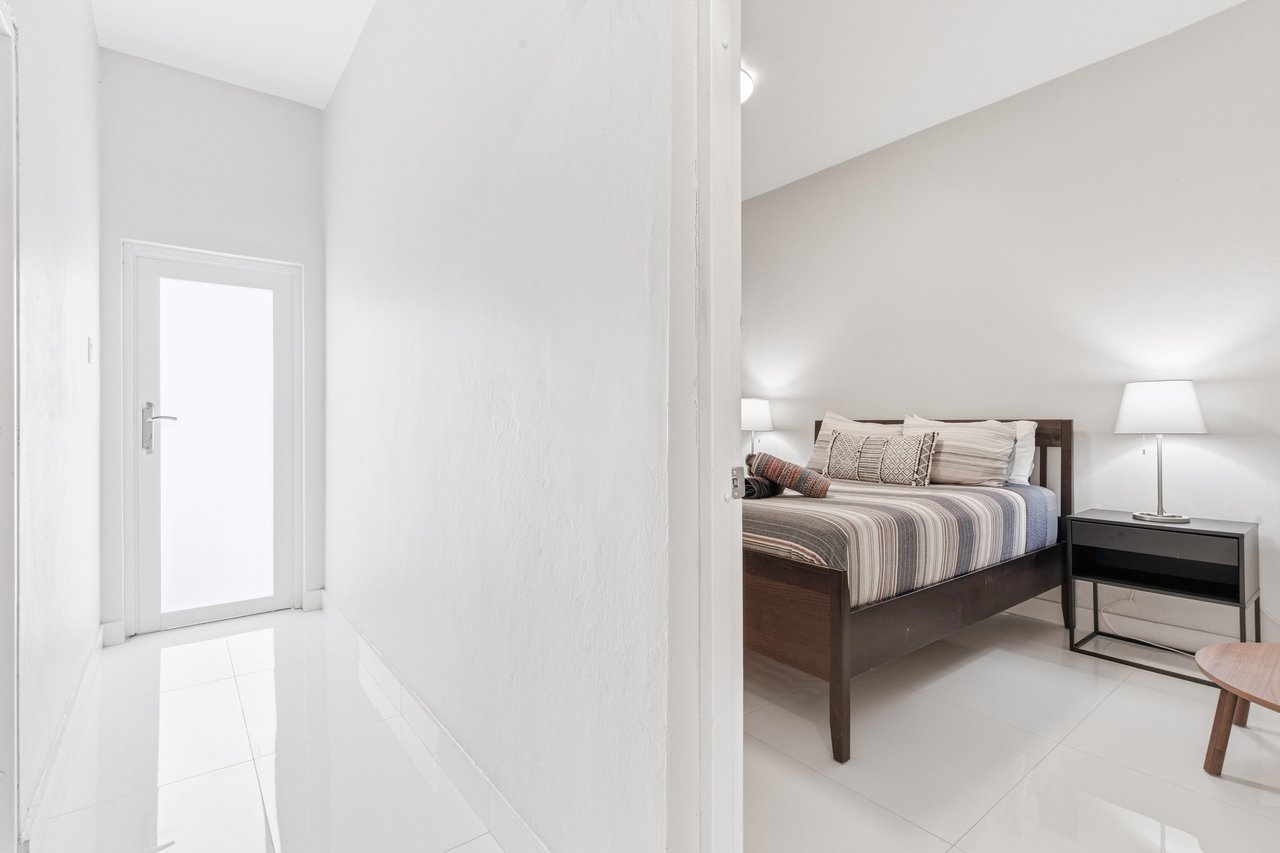 Bedroom with a dark wood bed, striped bedding, and black nightstand, viewed from a white-tiled entry hall.