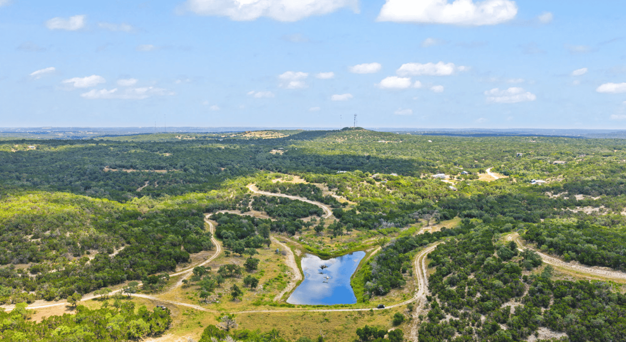 Aerial view of wooded ranchland with winding dirt roads and a small pond.