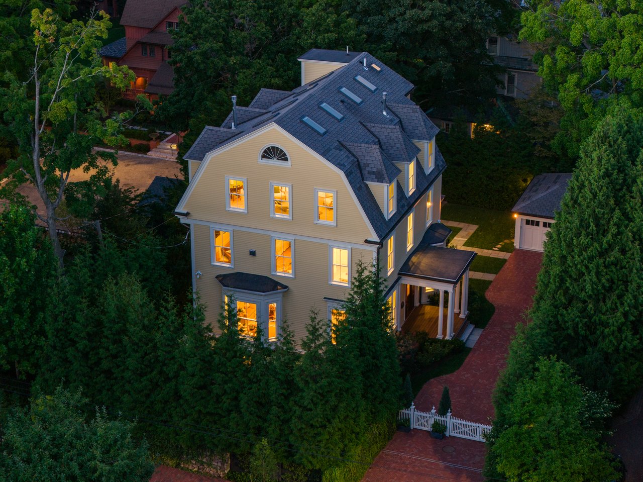 Aerial view of a Victorian house with a slate roof, glowing windows, and a brick driveway.