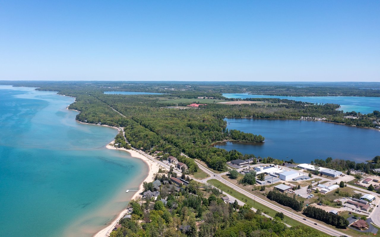 Aerial shoreline with sandy beaches, wooded land, and blue water on both sides.