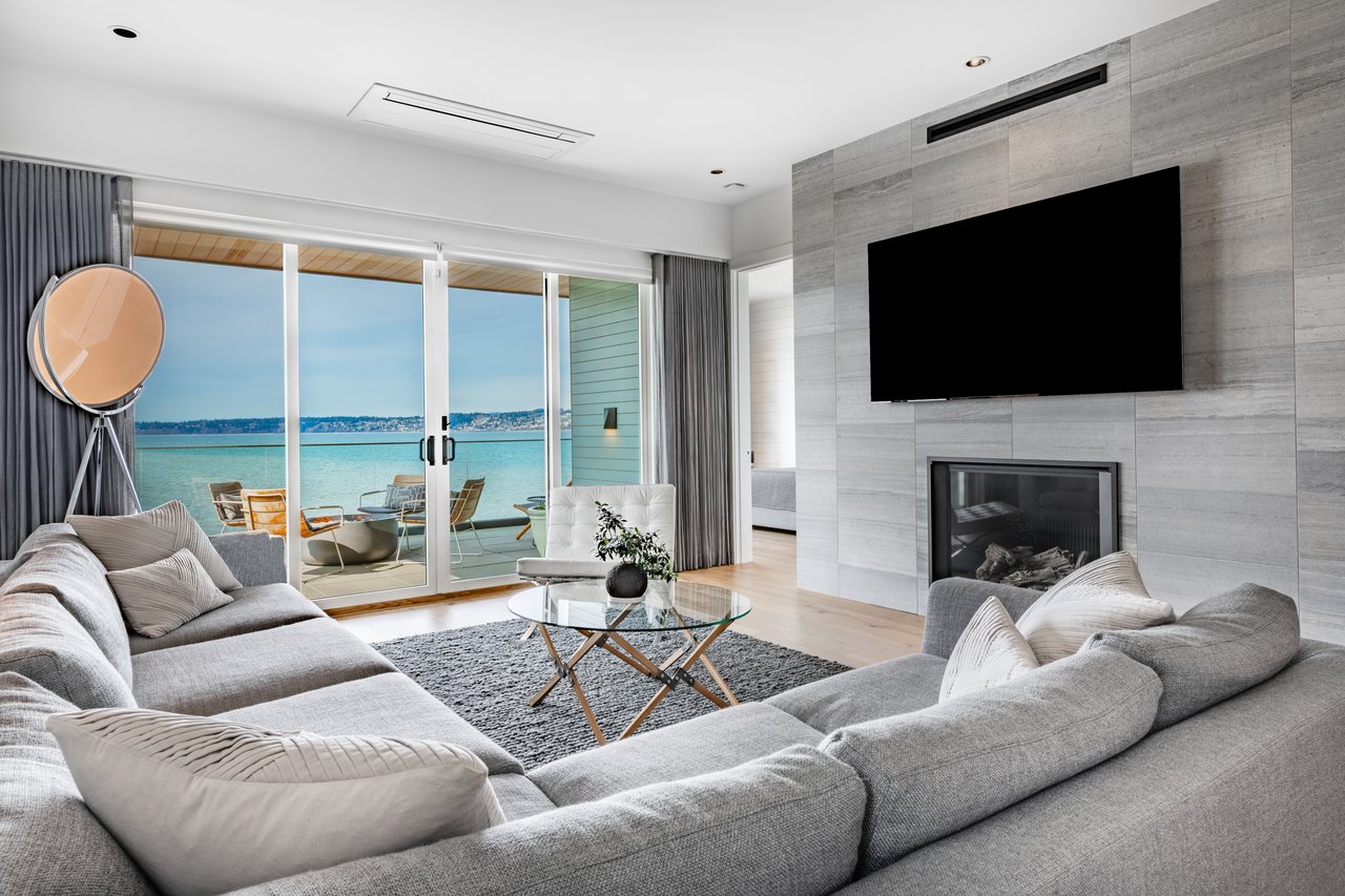 Modern living room with gray sectional sofas and sliding doors overlooking the water.
