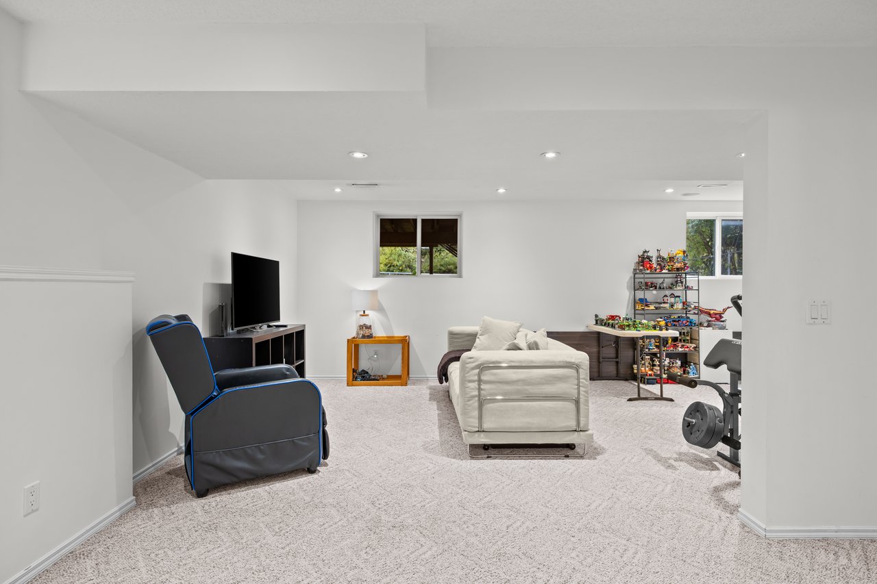 Basement recreation room with a white sofa, television, toy shelves, and exercise equipment.
