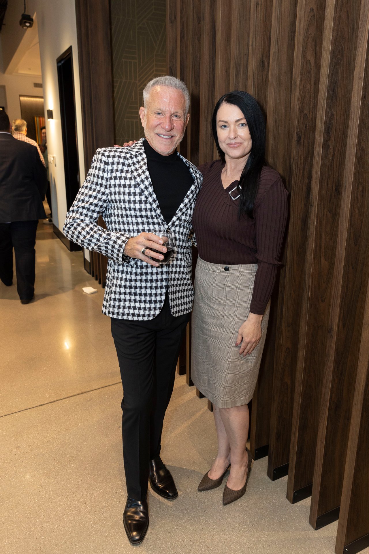 A man holding a drink poses beside a woman at an indoor open house.