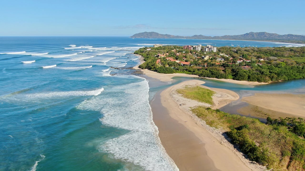 Aerial view of a tropical resort coastline with surf, sandy beach, and a river estuary.