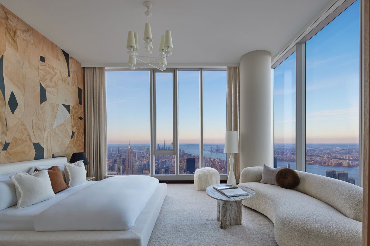 High-rise bedroom with a curved cream sofa and panoramic Manhattan skyline views.
