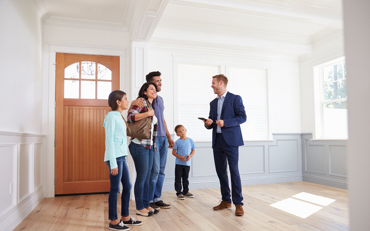 Family meets a real estate agent in a bright, empty room with hardwood floors.